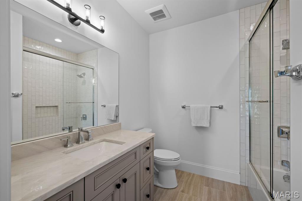 Bathroom with a pale stone vanity, large mirror, and glass-enclosed tiled shower.