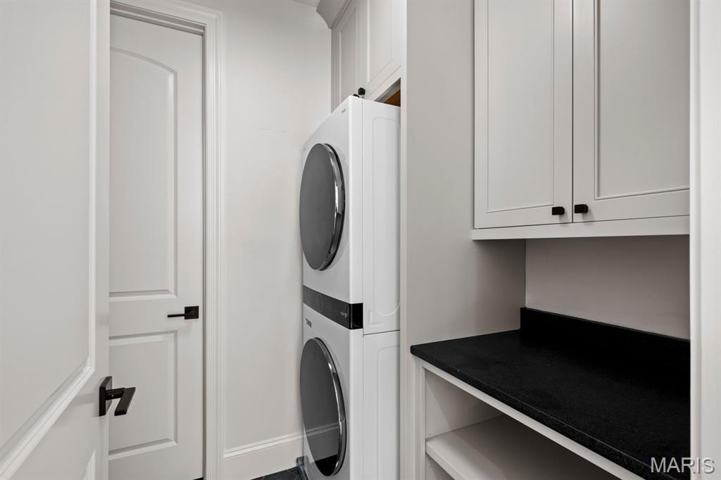 Laundry room with stacked washer and dryer, white cabinets, and a black countertop.