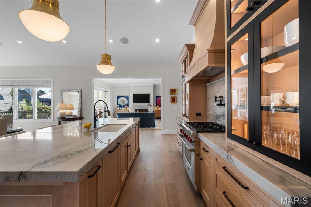 Bright kitchen with a marble island, light wood cabinets, and glass-front display cabinets.