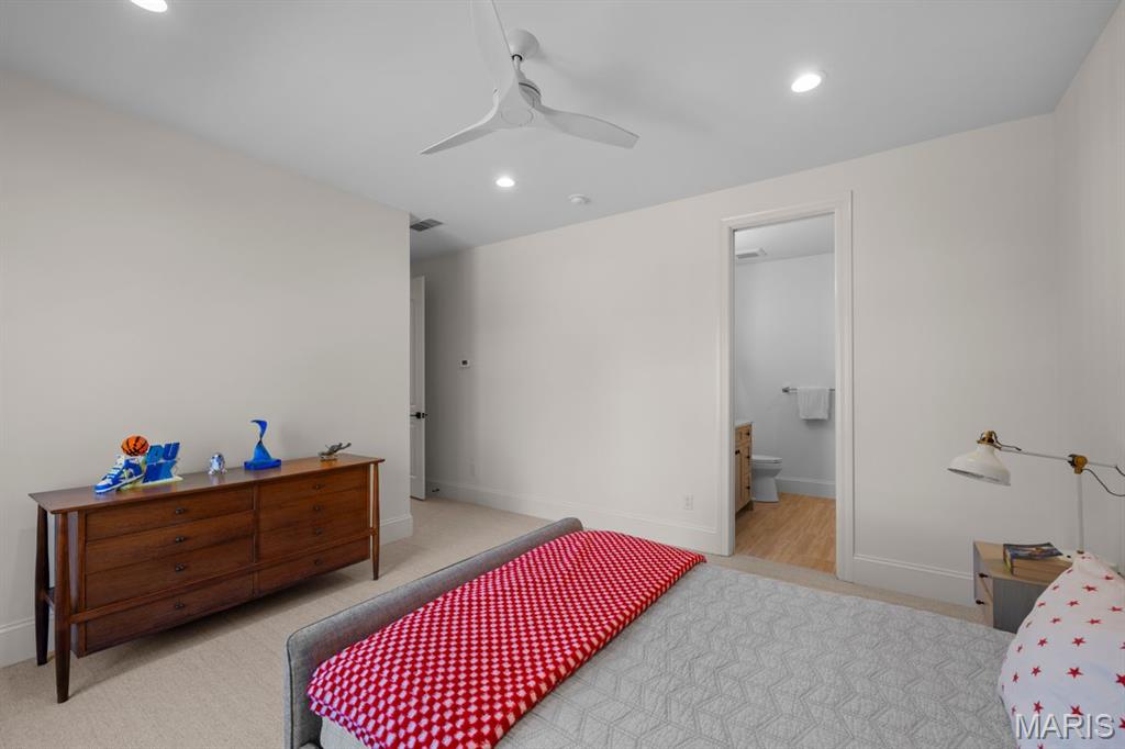 Bedroom with a red patterned bed runner, wooden dresser, and open doorway to a bathroom.