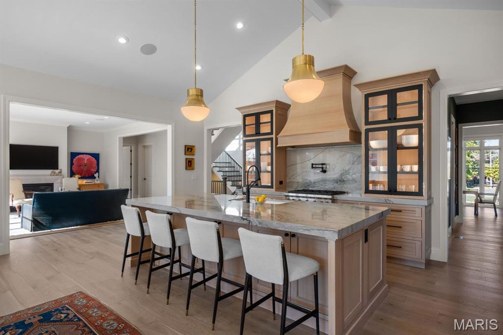 Kitchen with a marble island, white stools, wood range hood, and adjoining living room.