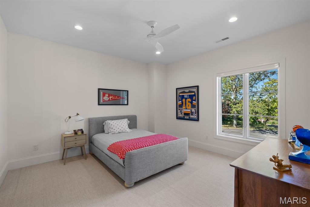 Bedroom with gray upholstered bed, red-and-white bedding, and a large window overlooking leafy trees.