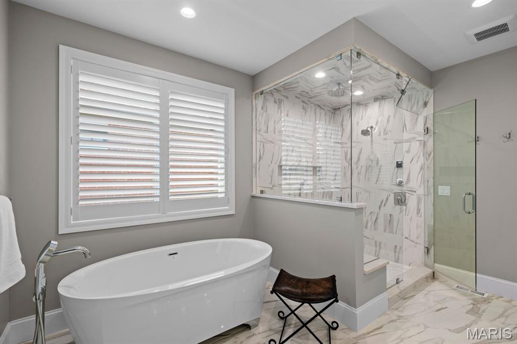 Bathroom with a freestanding tub and marble-tiled glass shower beside a shuttered window.
