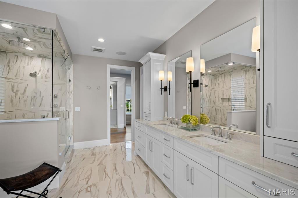 Bathroom with a glass-enclosed marble shower and long double vanity with large mirrors.