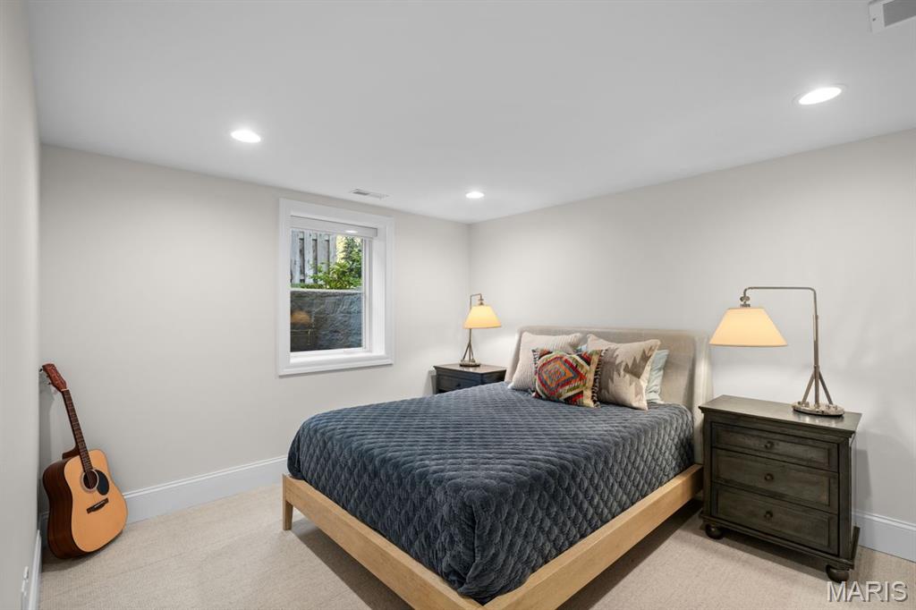 Staged bedroom with a dark blue quilted bed, bedside lamps, a window, and an acoustic guitar.