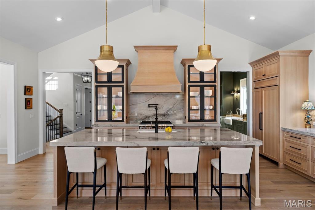 Kitchen with a large marble island, four bar stools, light wood cabinetry, and brass pendant lights.