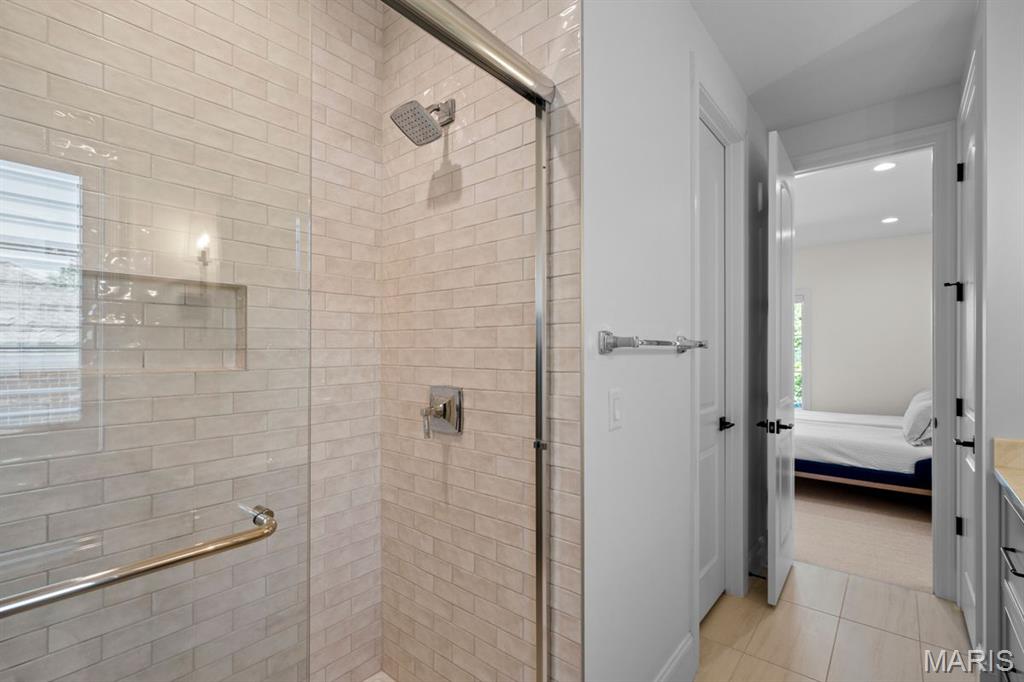 Tiled walk-in shower with glass doors and chrome fixtures, beside an open doorway to a bedroom.