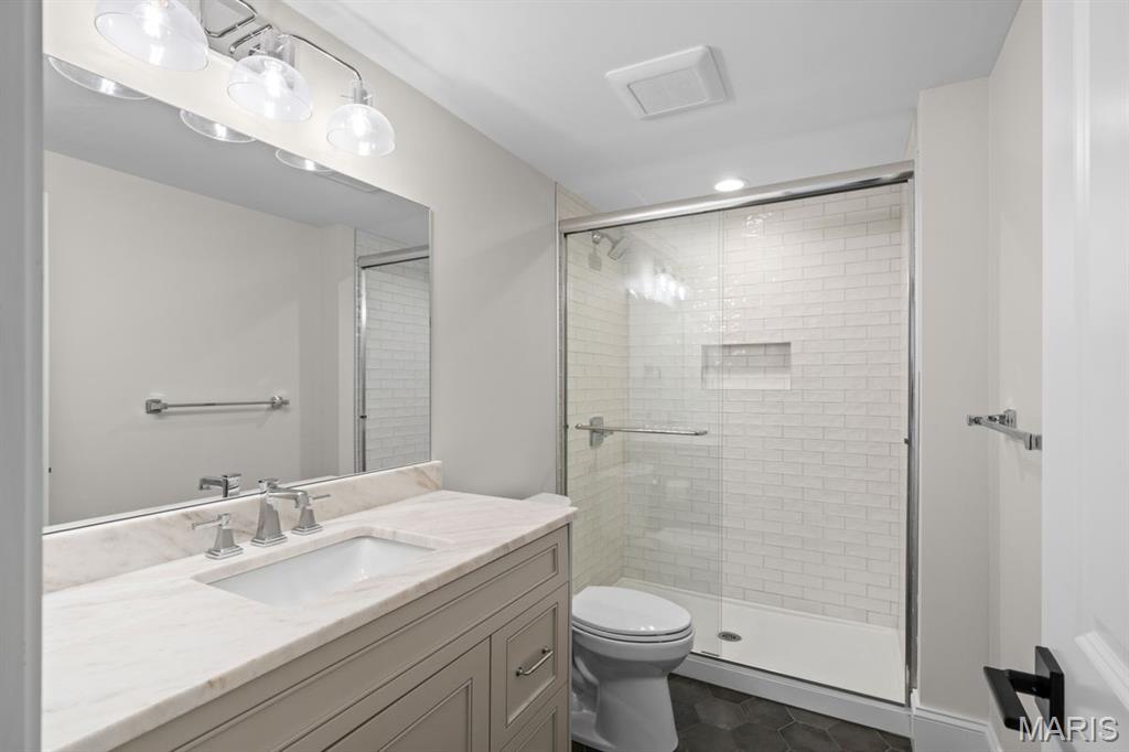 Bathroom with marble vanity and glass-enclosed white subway tile shower.