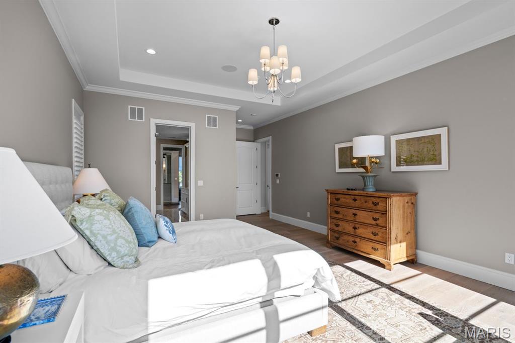 Bedroom with a white upholstered bed, tray ceiling, chandelier, and wooden dresser.
