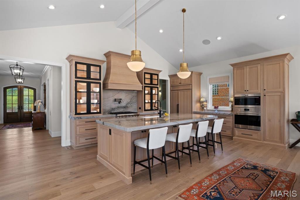 Kitchen with a marble island, five white stools, light wood cabinetry, and a patterned rug.