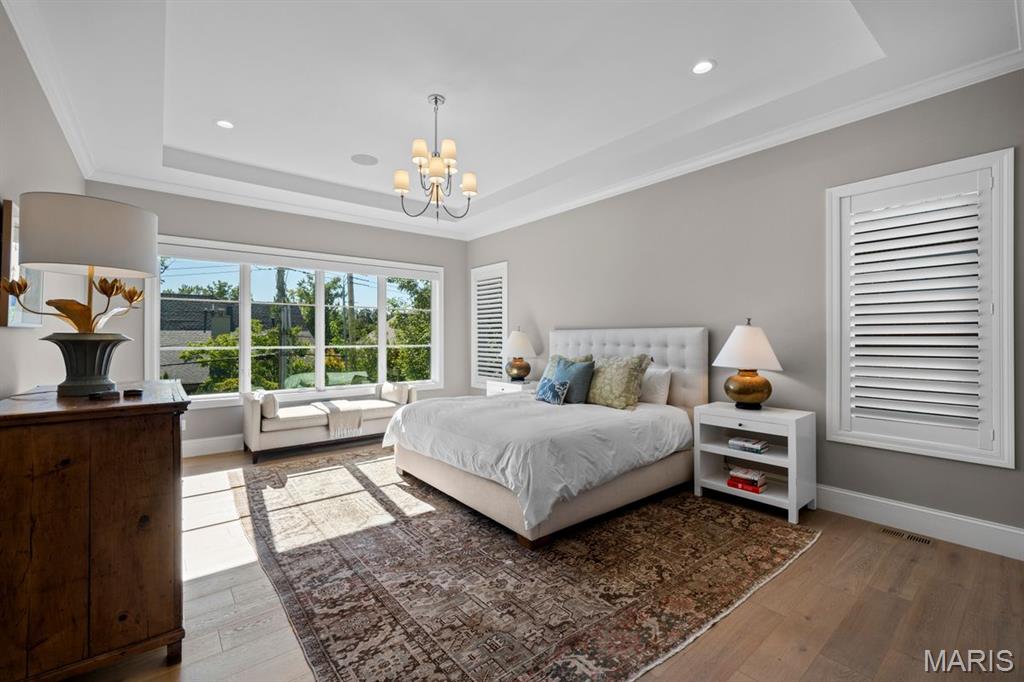 Bedroom with a white upholstered bed, large garden-facing window, window seat, and patterned rug.
