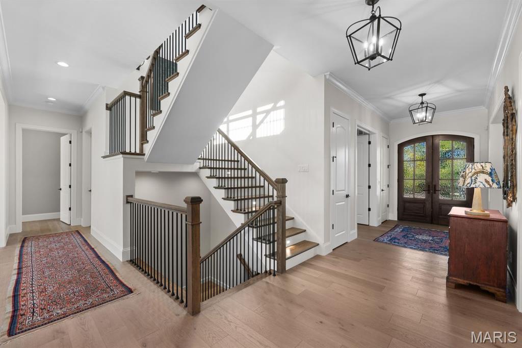 Entry foyer with a staircase, patterned rugs, and dark glass-paneled double doors.