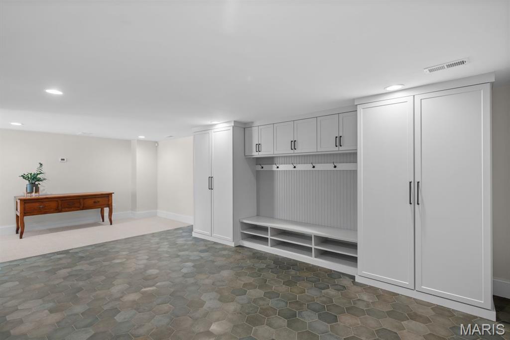 Built-in storage room with white cabinets and coat hooks above gray hexagonal tile flooring.