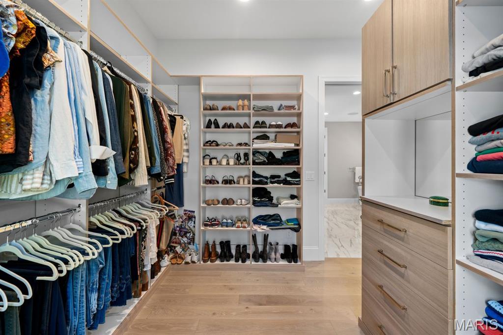 Walk-in closet with built-in cabinetry, shoe shelves, and clothing on hanging rails.