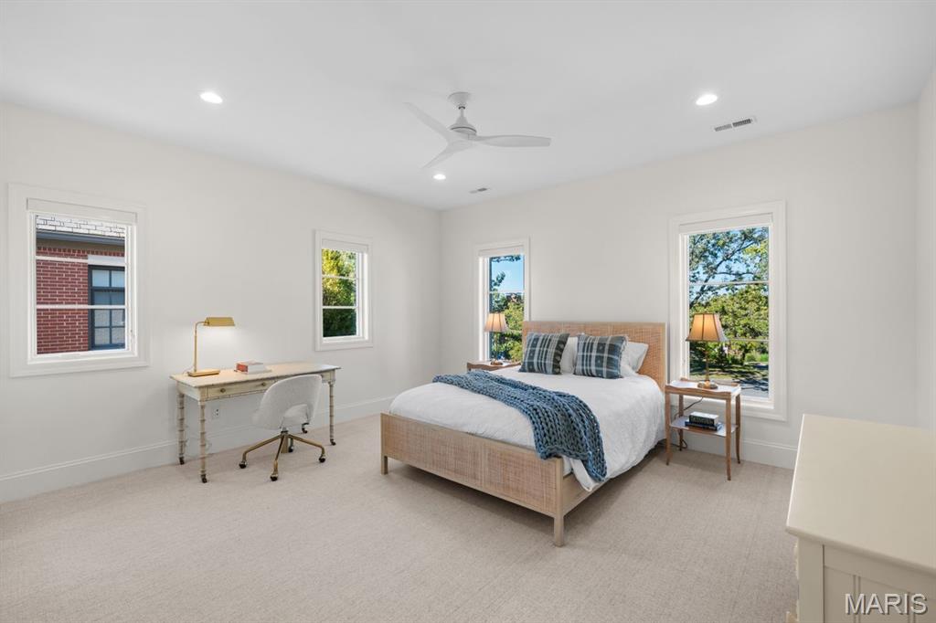 Furnished bedroom with a light upholstered bed, blue throw, desk, and multiple windows.