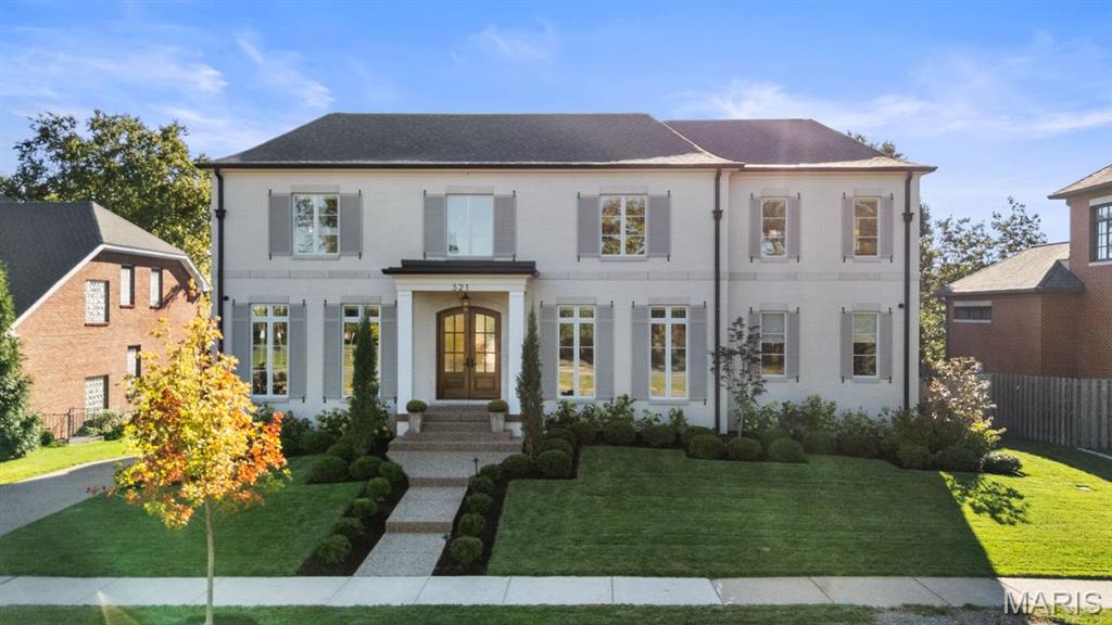 White two-story house with gray shutters, an arched front door, and a landscaped front lawn.