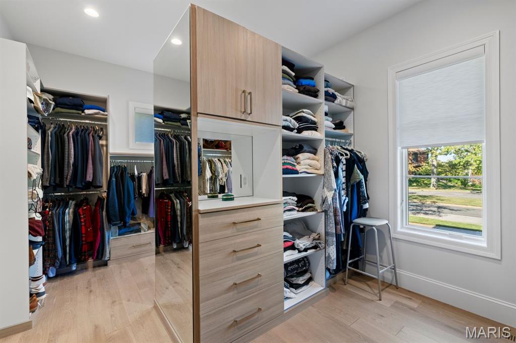 Walk-in closet with mirrored cabinetry, organized clothes, and a large window overlooking a leafy street.