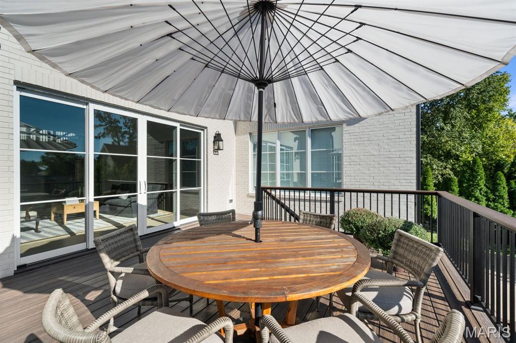 Outdoor deck with a round wooden dining table beneath a large white umbrella.