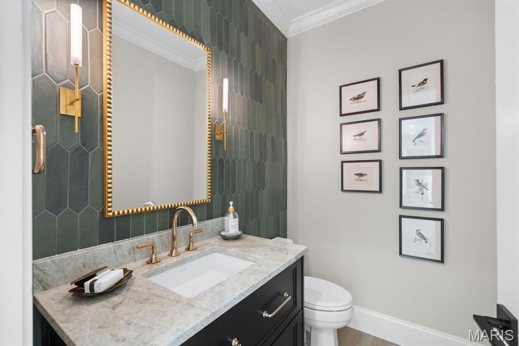 Bathroom vanity with green tile, a gold-framed mirror, brass fixtures, and framed bird prints.
