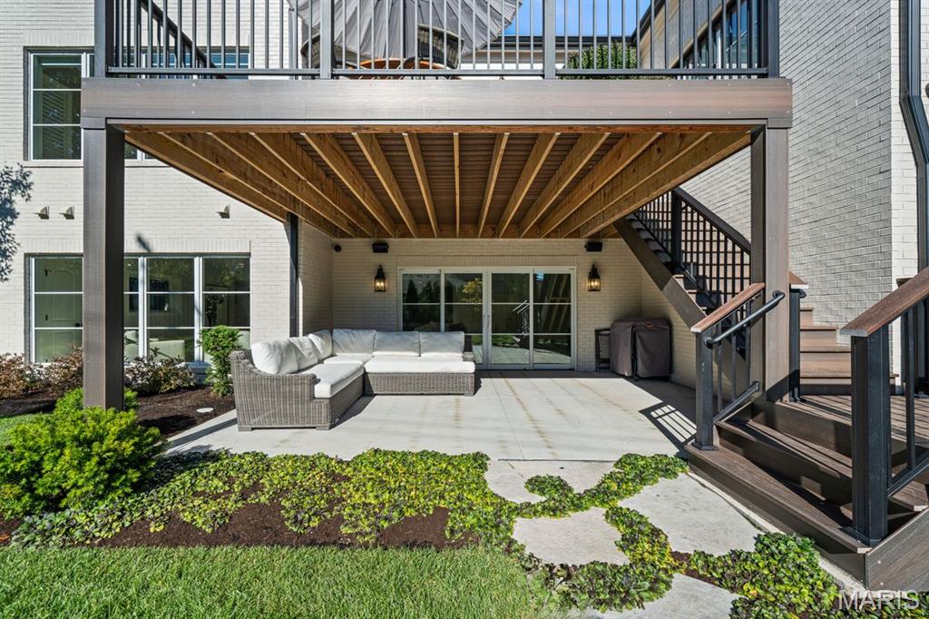 Covered patio with a white sectional, wood ceiling, sliding glass doors, and stairs to an upper deck.