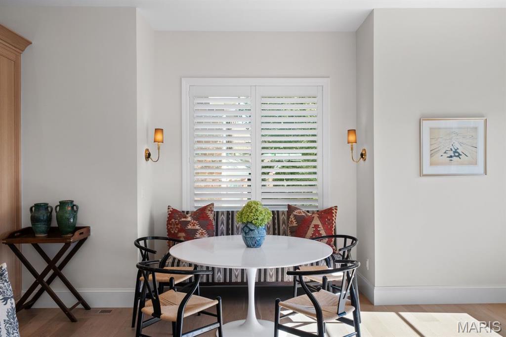 Dining nook with a white pedestal table, black chairs, and a striped bench beneath shuttered windows.