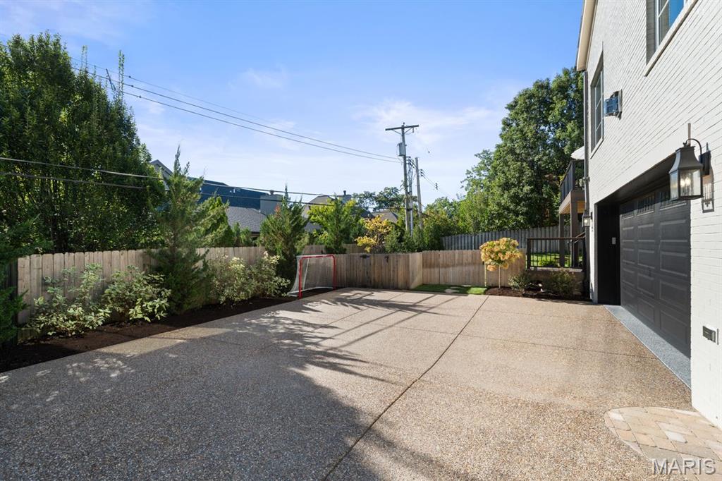 Paved courtyard beside a white-sided home, with a garage, fenced garden beds, and a small soccer goal.