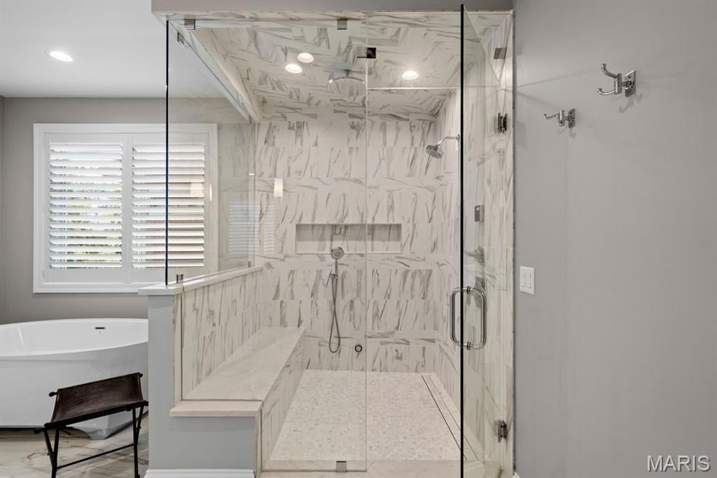Bathroom with a glass-enclosed marble-look shower, built-in bench, and freestanding tub.