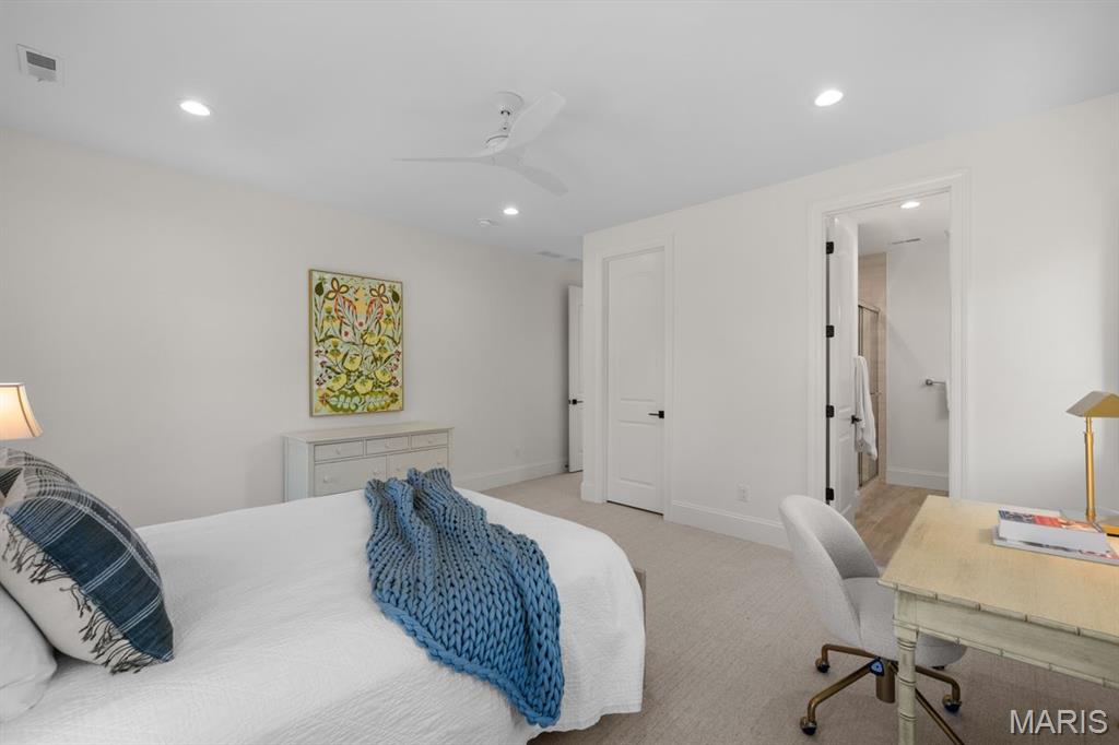 Staged bedroom with a blue knit throw, floral artwork, and an open doorway to the bathroom.