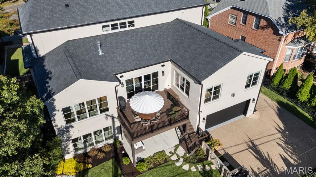 Aerial view of a light-colored home with a raised wooden deck, white umbrella, and attached garage.