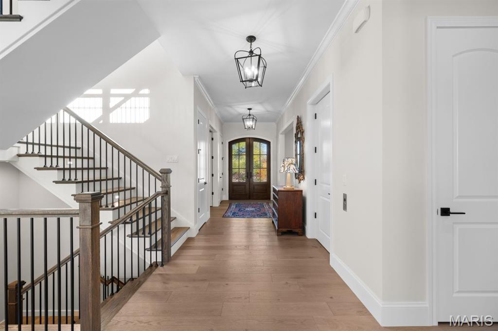 Bright entry hall with wood floors, a dark-railed staircase, and glass double front doors.