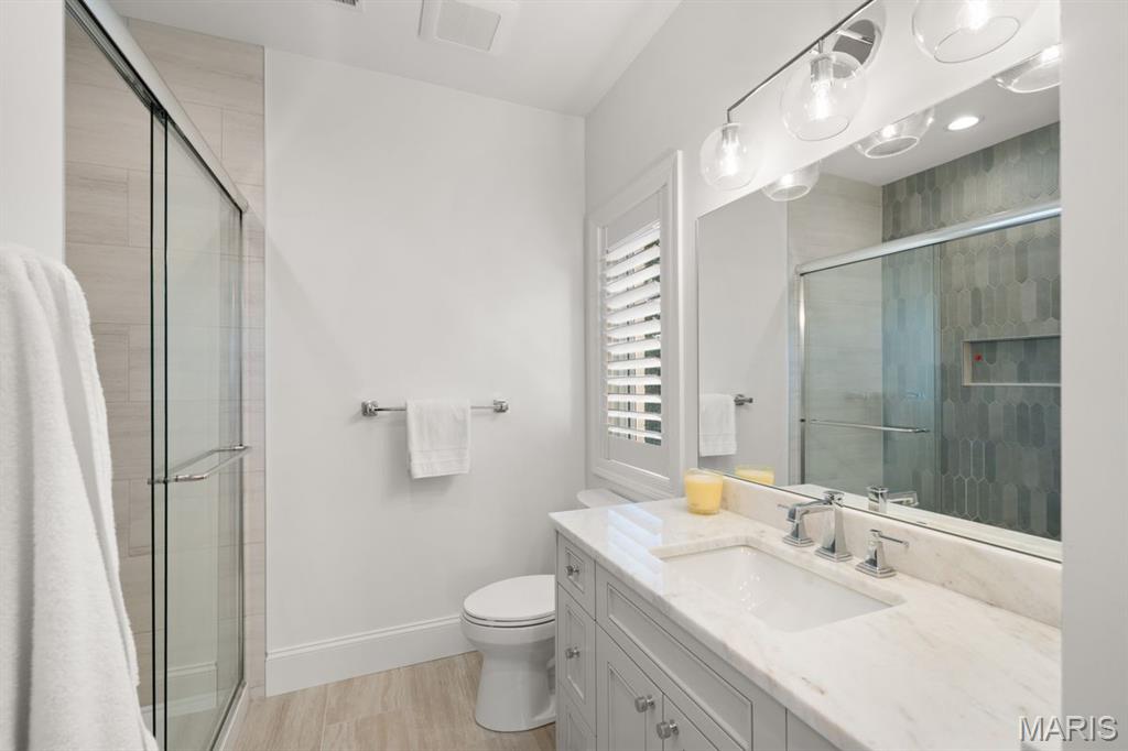 Bathroom with a glass shower, gray hexagonal tile, and a white vanity with marble countertop.