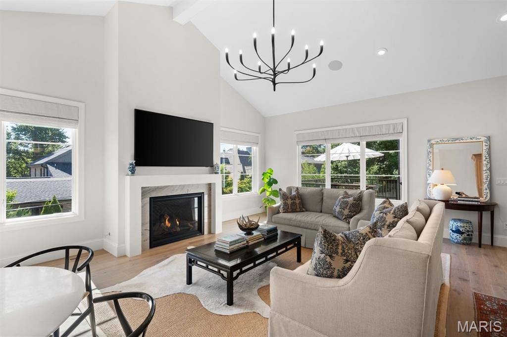 Living room with a fireplace, wall-mounted TV, large windows, and neutral seating.