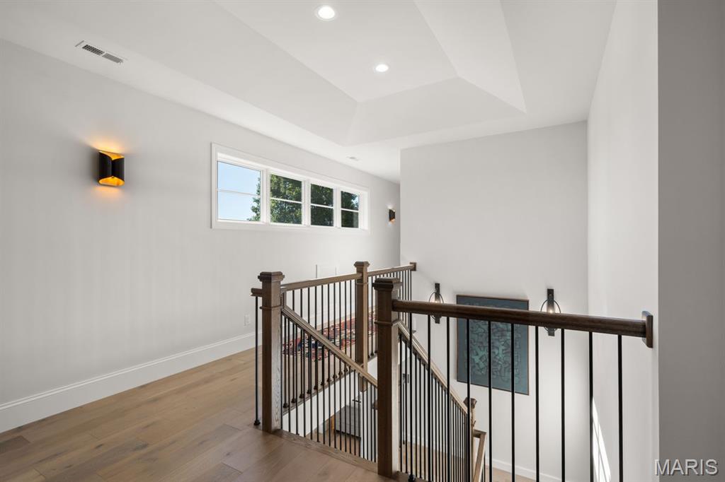 Upper landing overlooking a staircase, with dark railings, light wood floors, and high windows.