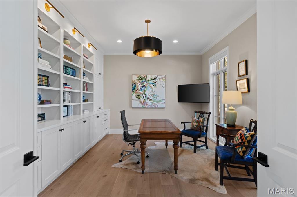 Furnished home office with built-in bookshelves, a wooden desk, and tall windows.