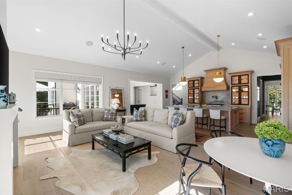 Staged living room opens to a kitchen, with a cream sectional and sculptural black chandelier.