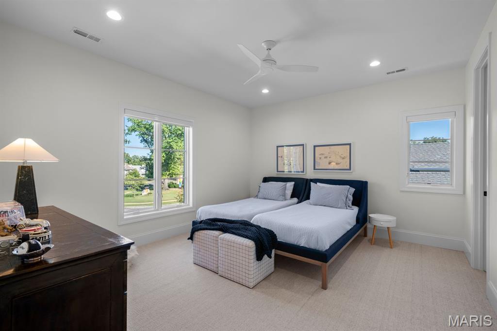 Bedroom with twin beds, navy headboards, a ceiling fan, and large windows overlooking greenery.
