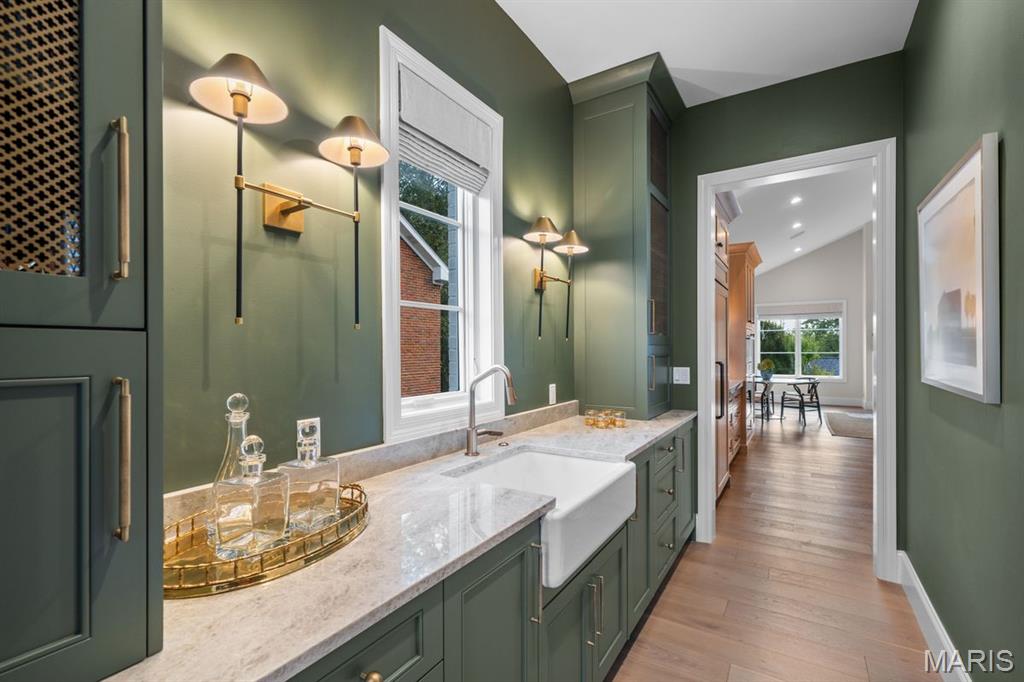 Green built-in cabinetry and stone counter with a farmhouse sink, opening onto a dining room.
