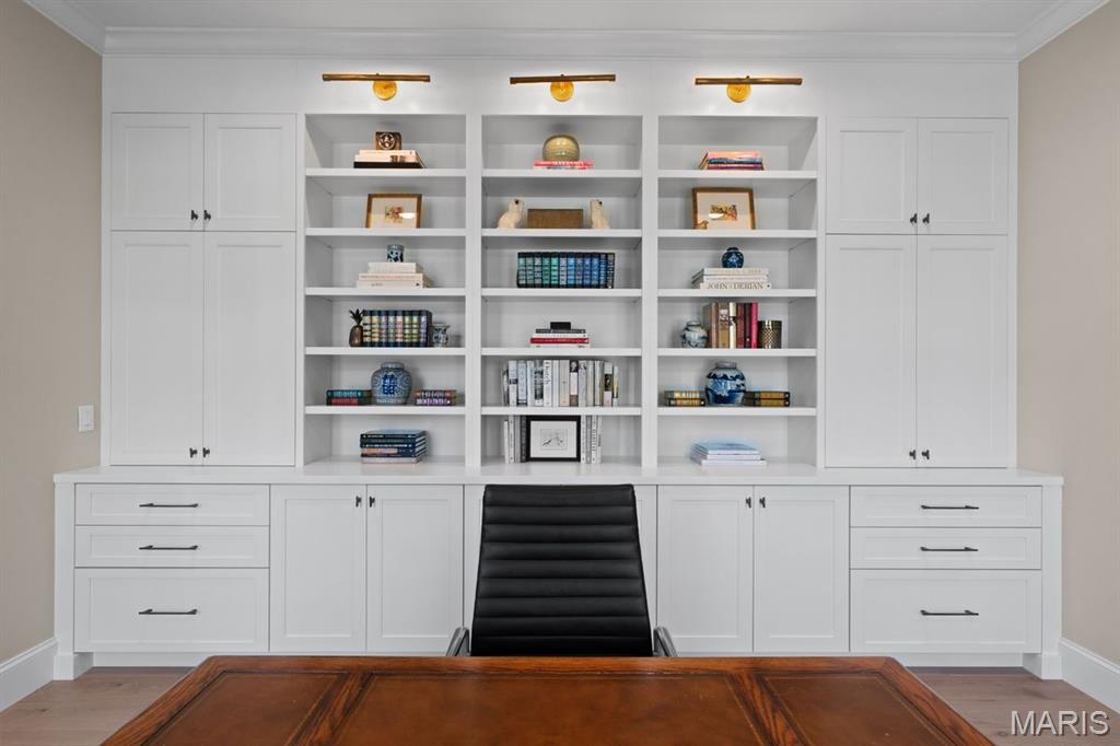 Home office with white built-in bookshelves, brass picture lights, and a large wooden desk.