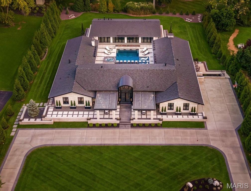 Aerial view of a large home with a central pool, landscaped grounds, and a curved driveway.