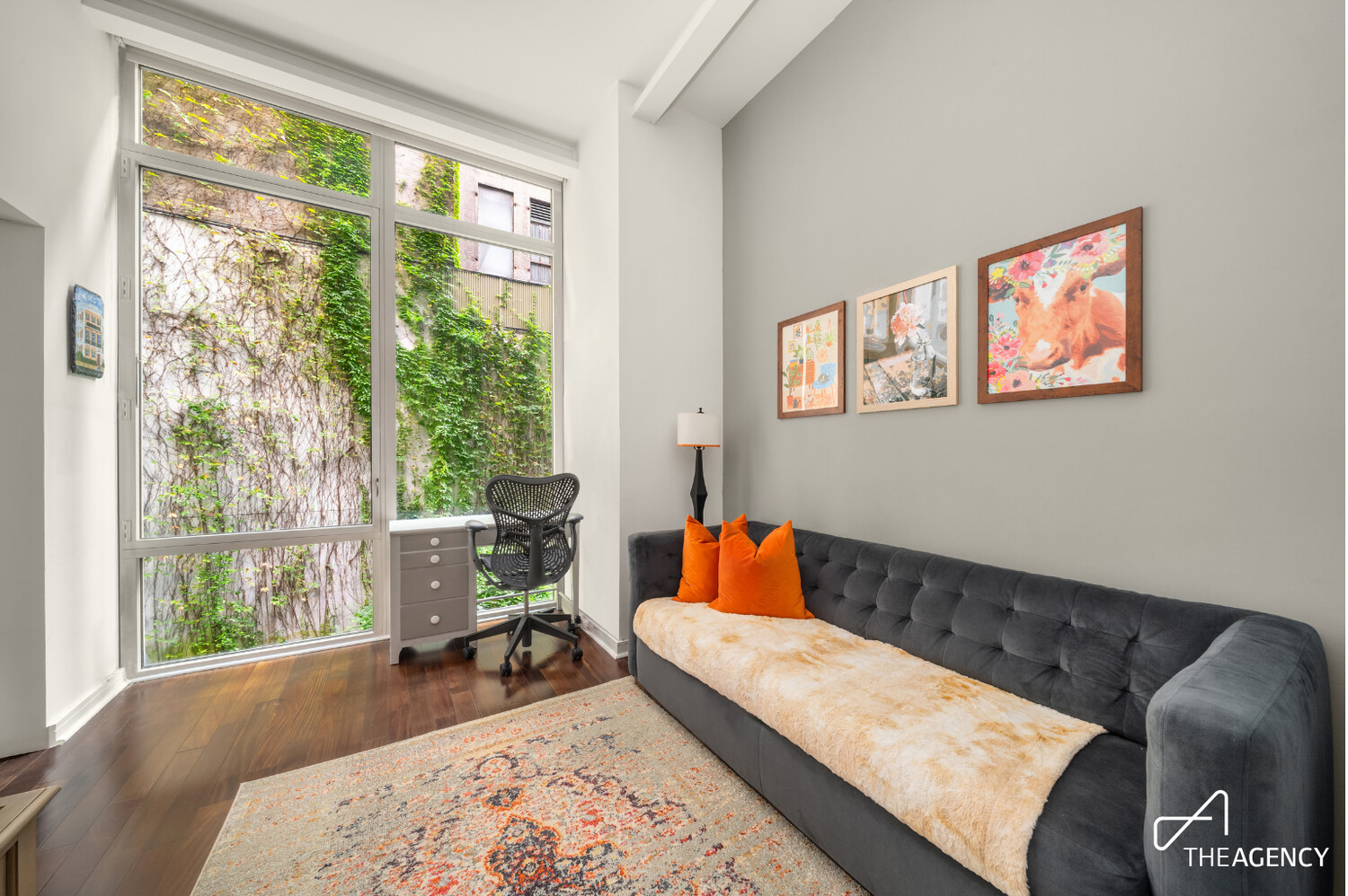 Living room with tall courtyard-facing windows, a dark tufted sofa, and bright orange cushions.