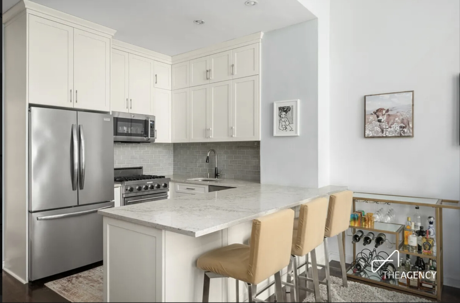 Kitchen with white cabinets, marble island, stainless steel appliances, and tan barstools.