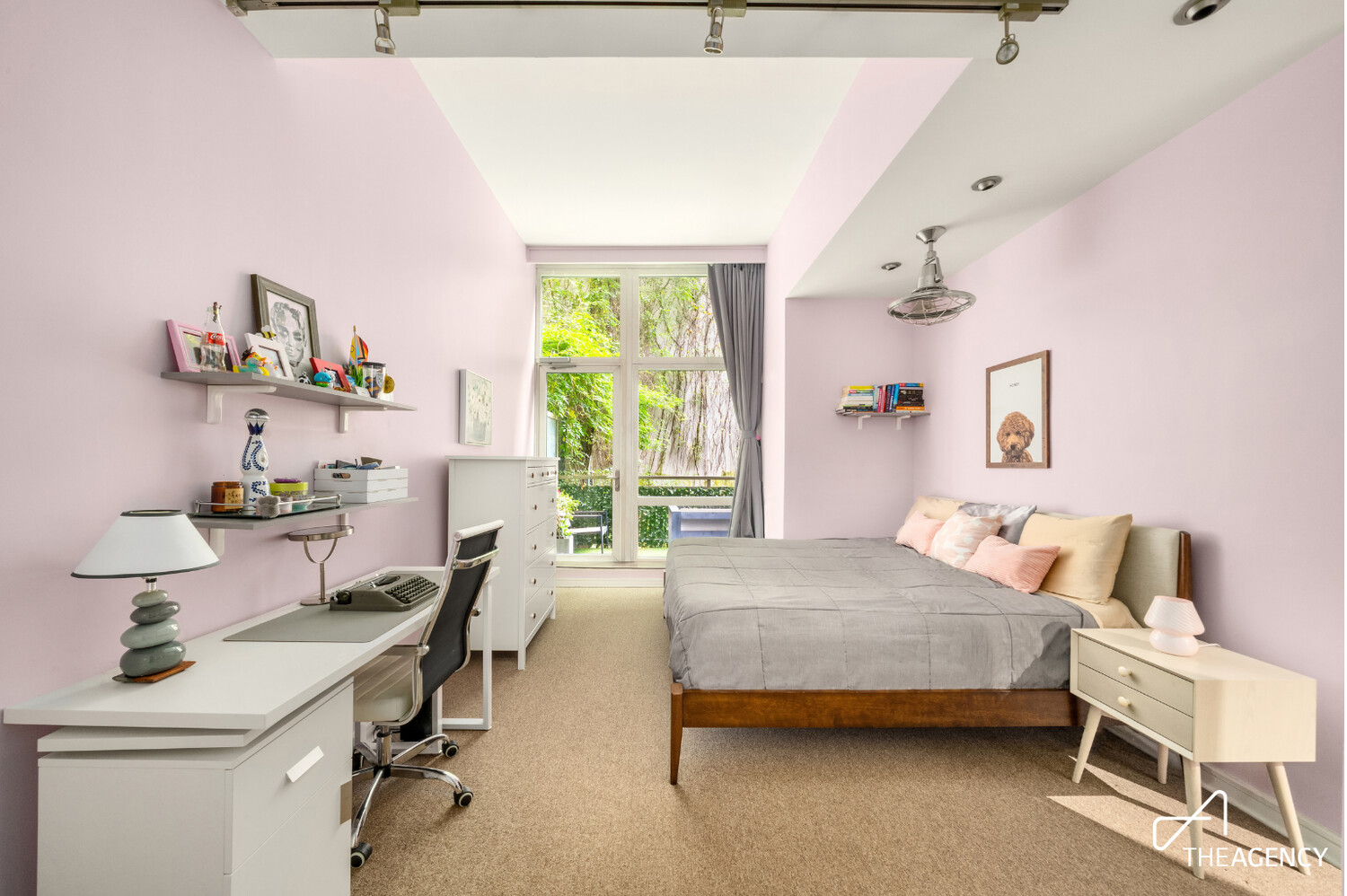 Furnished bedroom with pink walls, a gray bed, a desk, and a large window overlooking greenery.
