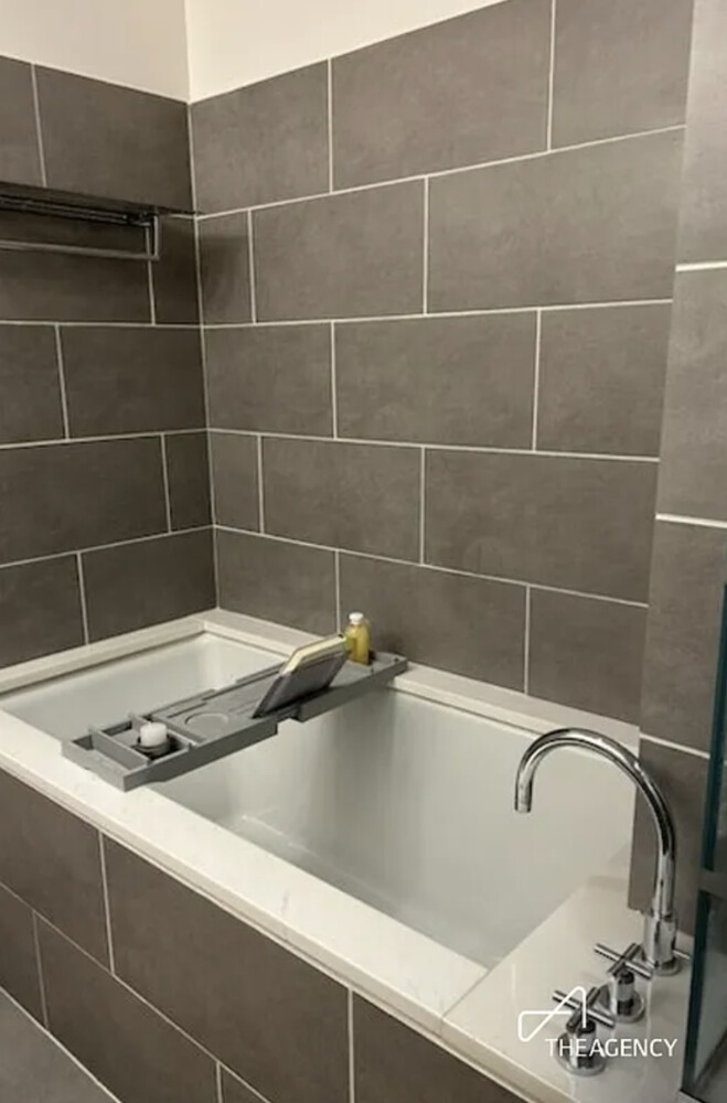 Bathroom bathtub with taupe-gray tile, a bath tray, and a chrome floor-mounted faucet.
