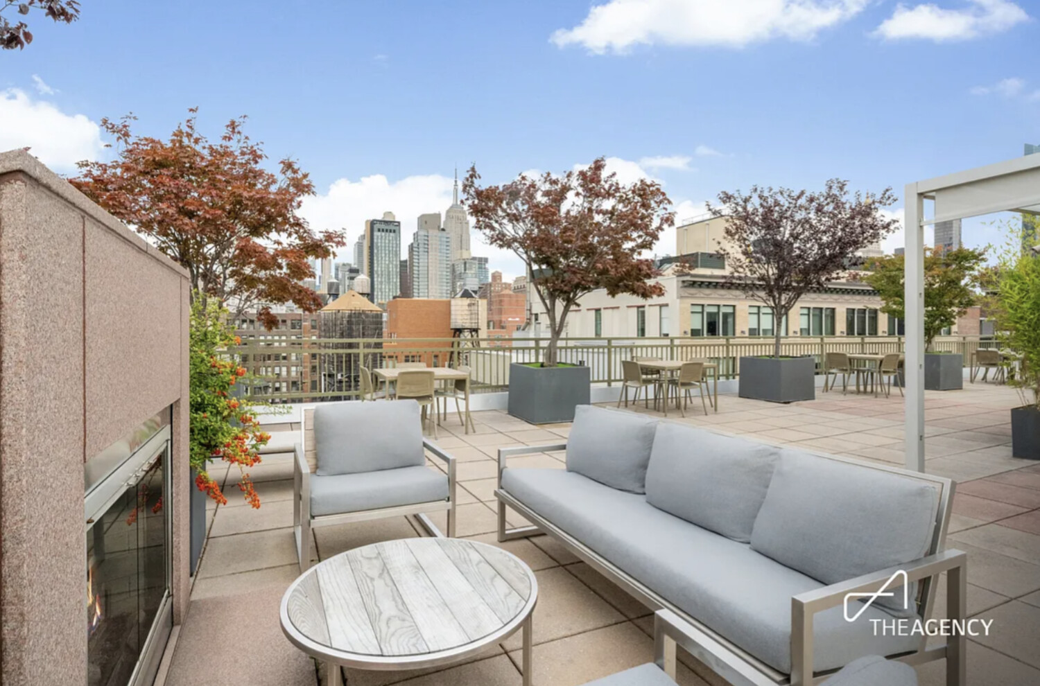 Rooftop terrace with gray lounge seating, a built-in fireplace, and Manhattan skyline views.