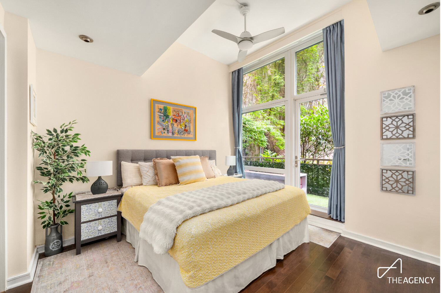 Furnished bedroom with a yellow bedspread and tall glass doors overlooking greenery.