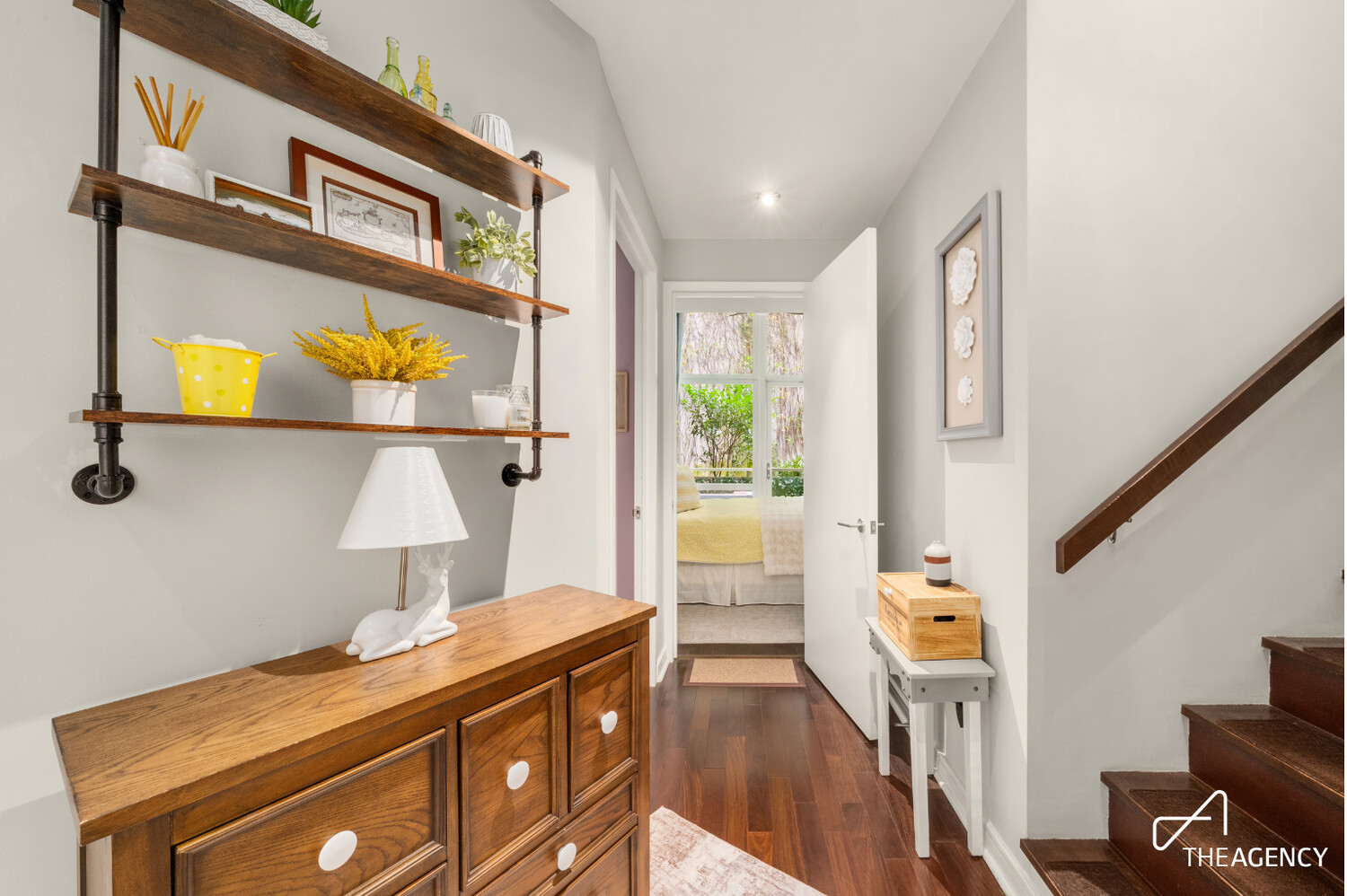 Furnished hallway with dark wood floors, decorative shelving, and stairs leading up beside the bedroom doorway.