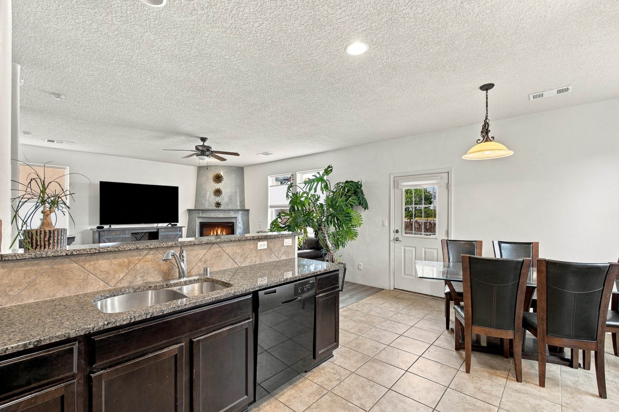 Open kitchen and dining area with granite counters, dark cabinets, and a fireplace in the adjoining living room.
