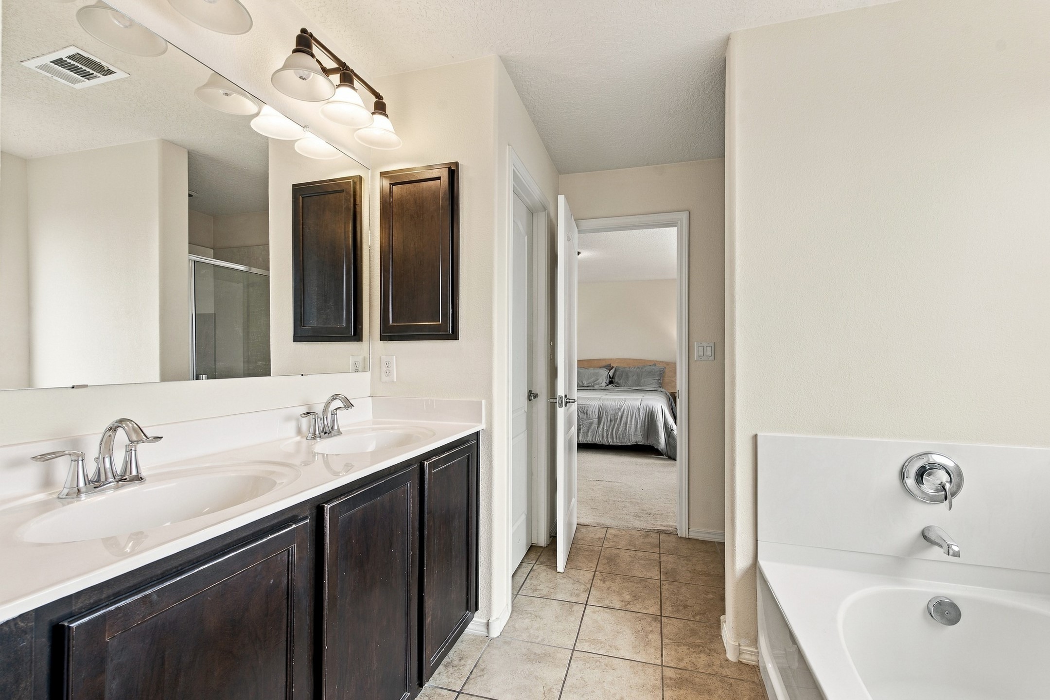 Bathroom with a dark double vanity and built-in tub, opening to a bedroom.