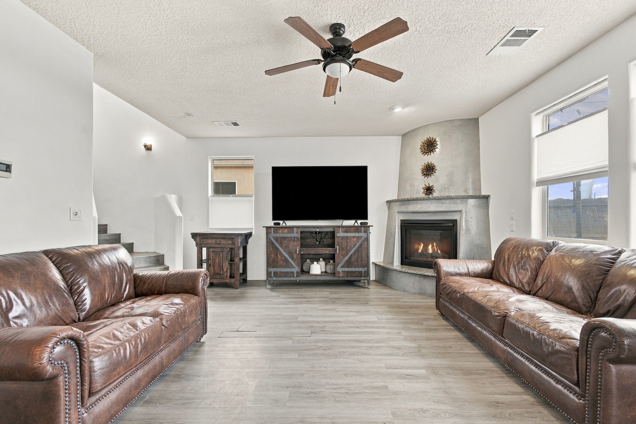 Living room with brown leather sofas, a lit fireplace, and a television above a rustic wood console.