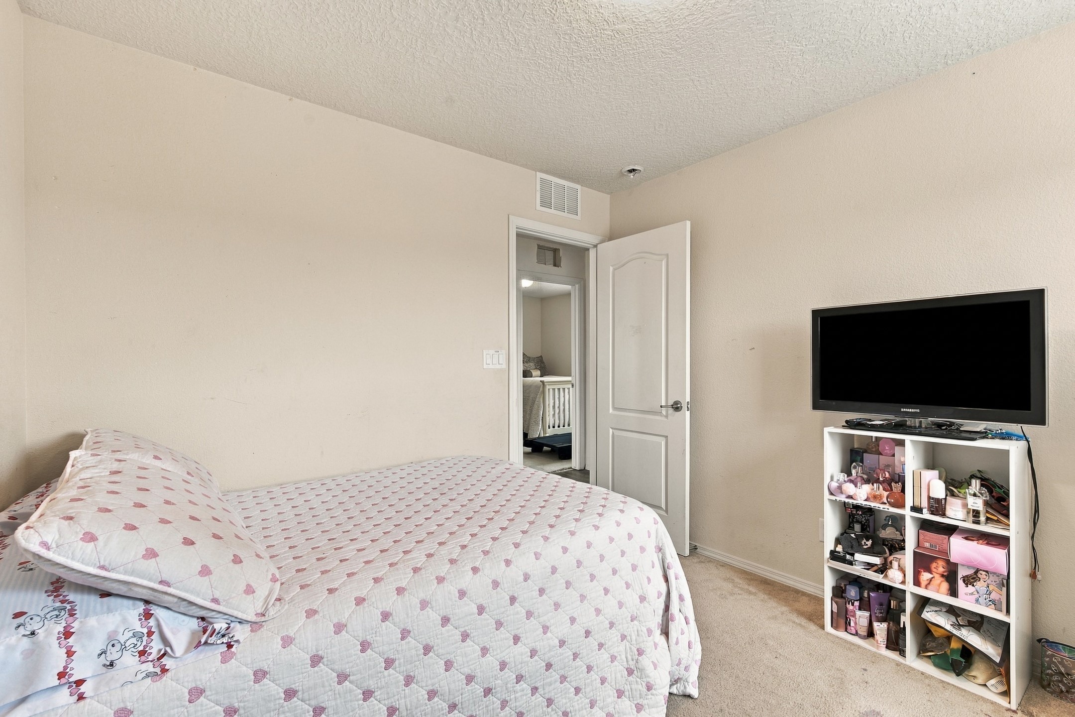 Bedroom with a pink heart-patterned quilt and a television above a crowded white cubby shelf.